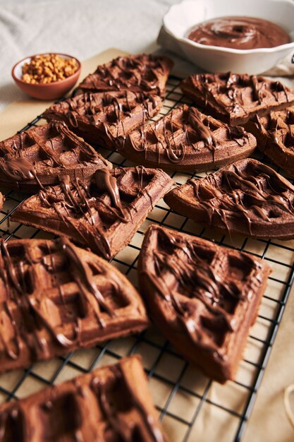 Foto vertical de deliciosos waffles de chocolate em uma rede na mesa perto dos ingredientes