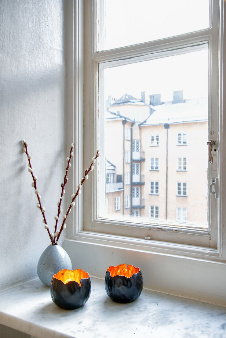 Foto grátis foto vertical de dois castiçais exclusivos e um vaso com uma planta de casa perto da janela