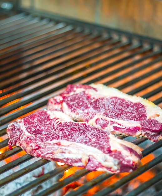 Foto vertical de fatias de carne crua cozinhando em chamas de fogo