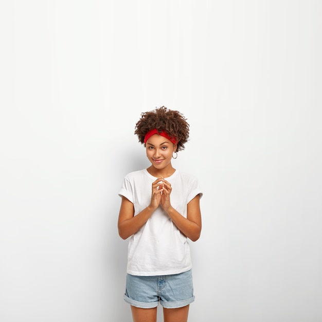 Foto grátis foto vertical de garota afro satisfeita faz um bom plano, mantém as mãos juntas