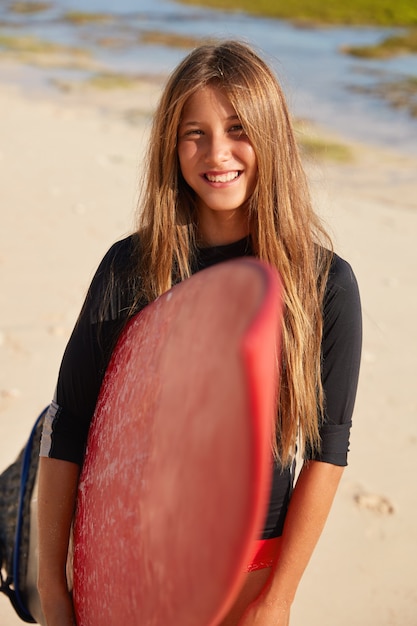 Foto vertical de jovem satisfeito com sorriso dentuço, vestindo roupa de mergulho preta