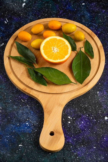 Foto vertical de meia laranja cortada com folhas e kumquats.