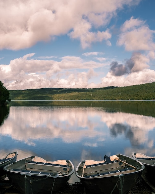 Foto vertical de pequenos barcos na margem de um lago com o reflexo do céu na superfície da água