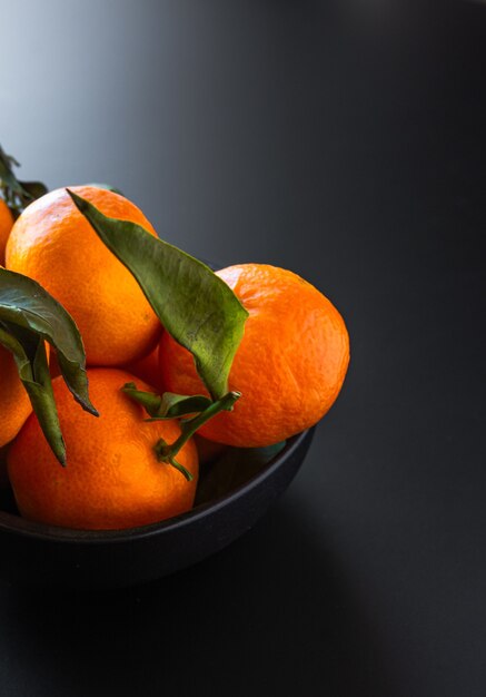 Foto vertical de tangerinas com folhas verdes em preto