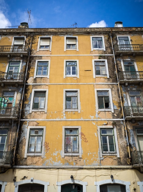 Foto vertical de um antigo prédio de apartamentos pintado de amarelo com algumas janelas quebradas