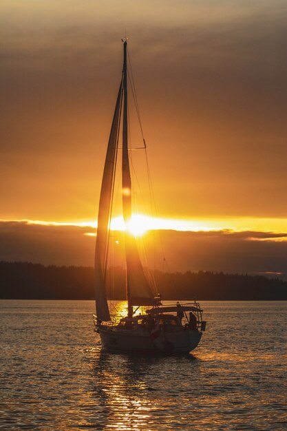 Foto vertical de um barco à vela no oceano durante o pôr do sol