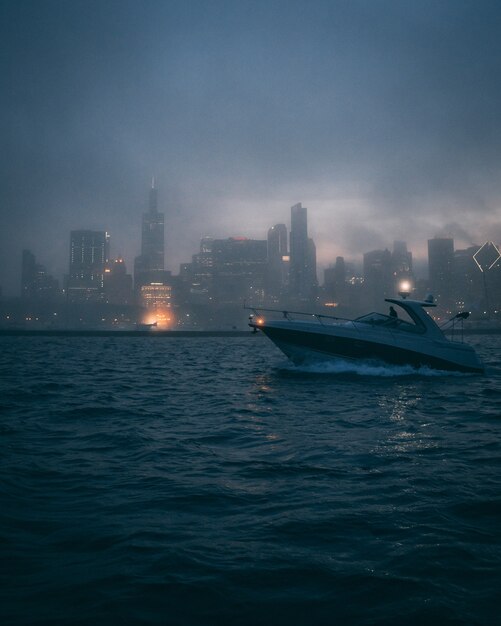 Foto vertical de um barco no oceano com as silhuetas de edifícios altos