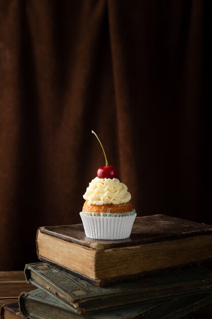 Foto vertical de um bolinho delicioso com creme e cereja no topo dos livros