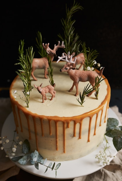 Foto vertical de um bolo de sonho com creme branco e gota de laranja com uma floresta e renas no topo