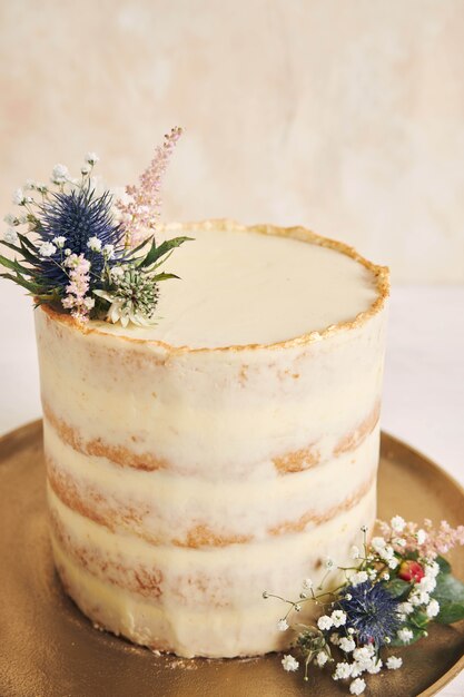 Foto vertical de um bolo lindo e delicioso com flores e bordas douradas em um fundo branco