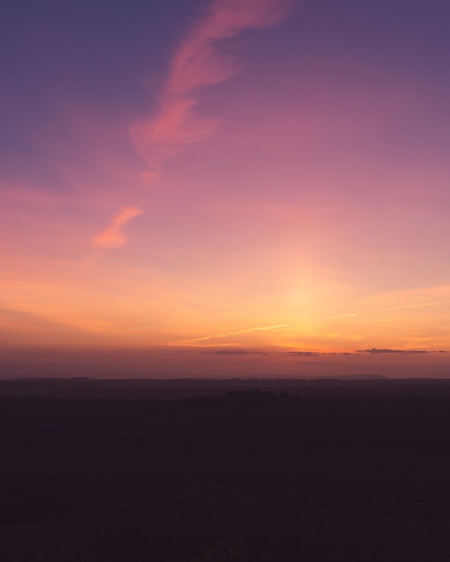 Foto vertical de um campo sob um céu roxo de tirar o fôlego