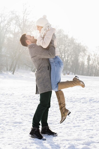 Foto vertical de um casal feliz curtindo a bela neve em um dia frio de inverno