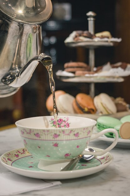 Foto vertical de um chá servindo em uma xícara sobre uma mesa de mármore com sobremesas