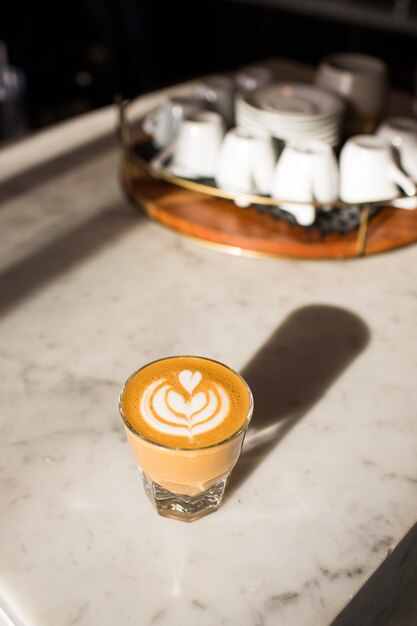 Foto vertical de um copo de café com leite na mesa sob as luzes