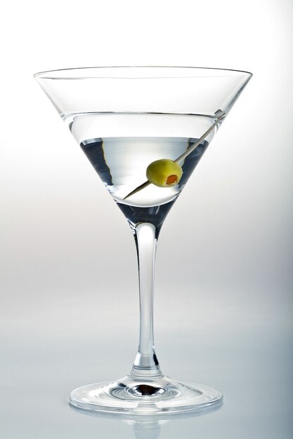 Foto vertical de um copo de Martini e uma azeitona em branco
