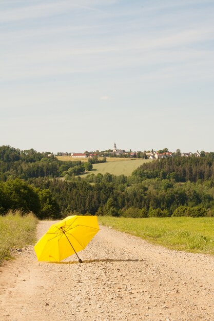 Foto vertical de um guarda-chuva amarelo aberto na estrada no campo