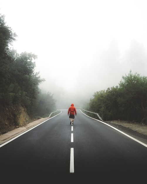 Foto vertical de um homem caminhando pela rodovia coberta por névoa