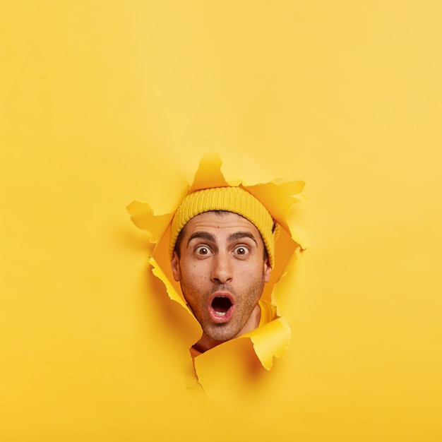 Foto vertical de um homem com a barba por fazer estupefato olhando para a câmera