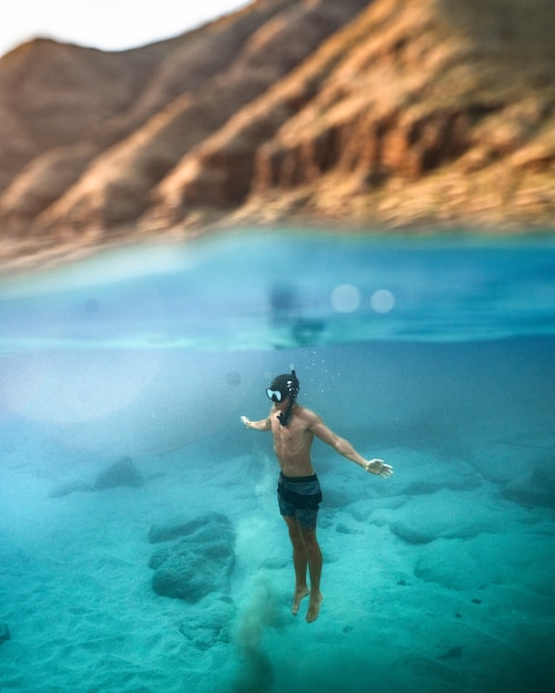 Foto vertical de um homem mergulhando no mar azul-turquesa