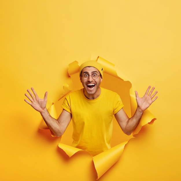 Foto vertical de um homem otimista posando através de um papel rasgado