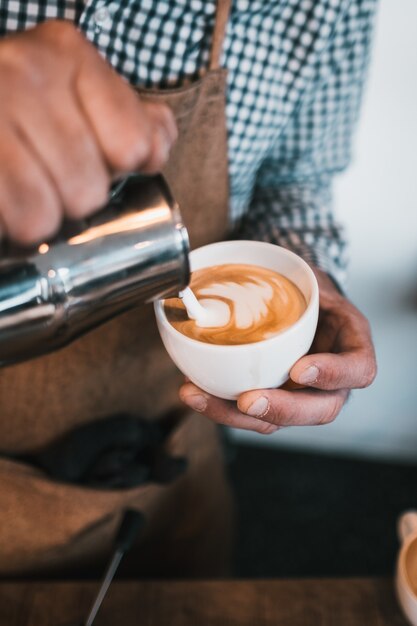 Foto vertical de um homem servindo leite em uma xícara de cappuccino em um café