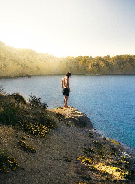 Foto vertical de um homem solitário se preparando para pular no lago em um dia ensolarado