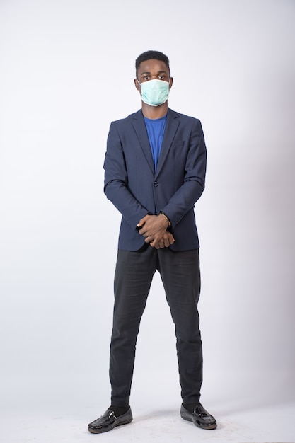 Foto vertical de um jovem empresário negro vestindo um terno e também uma máscara facial, em pé com confiança