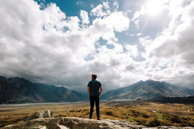 Foto vertical de um jovem homem olhando para as montanhas em um dia ensolarado