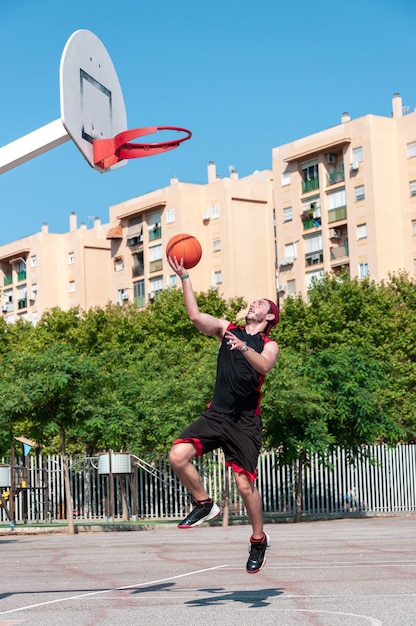 Foto vertical de um jovem jogando a bola na cesta de basquete