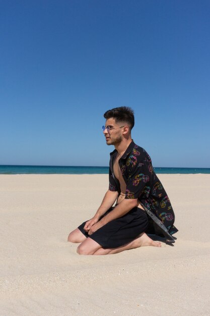 Foto vertical de um jovem sentado na areia na praia