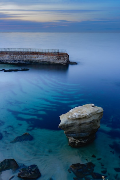 Foto vertical de um mar azul e cristalino de tirar o fôlego com uma cerca de pedra