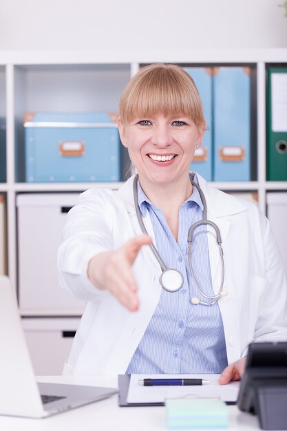 Foto vertical de um médico caucasiano feliz oferecendo cooperação com um aperto de mão