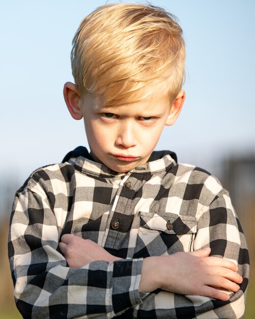 Foto vertical de um menino vestindo uma camisa de flanela com uma carranca fofa no rosto