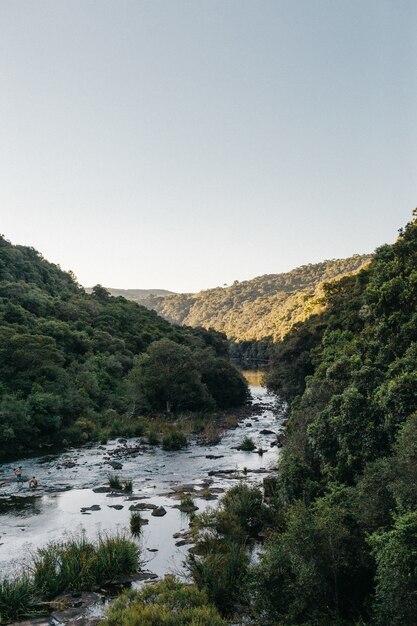 Foto vertical de um rio fluindo cercado por montanhas com céu claro