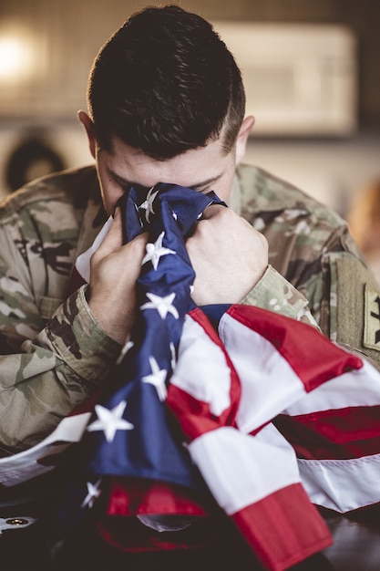 Foto vertical de um soldado americano em luto e orando com a bandeira americana nas mãos
