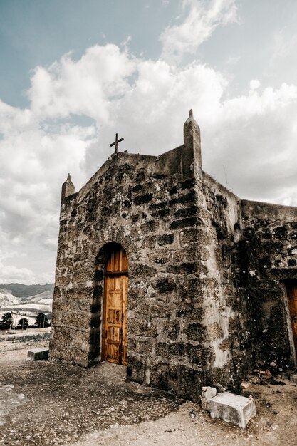 Foto vertical de uma igreja antiga com porta de madeira e paredes em ruínas durante o dia