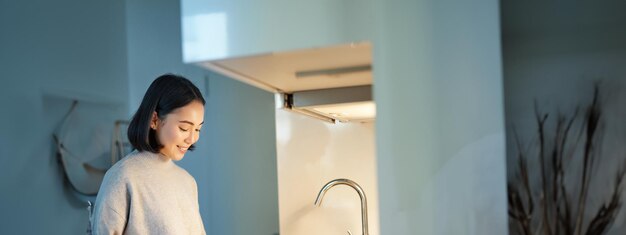 Foto grátis foto vertical de uma jovem asiática cozinhando o jantar fazendo-se sandwitch sorrindo enquanto estava em pé