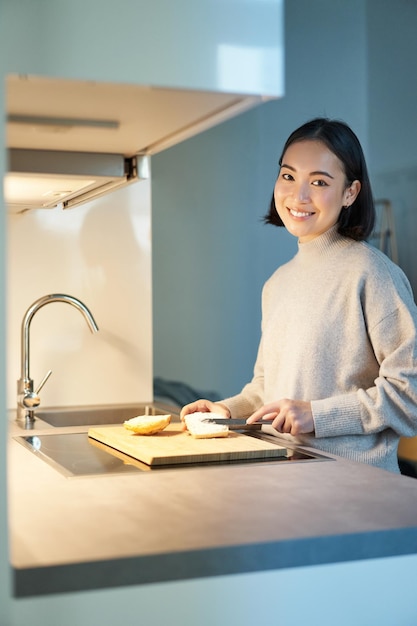 Foto grátis foto vertical de uma jovem asiática preparando o jantar fazendo-se sandwitch sorrindo em pé