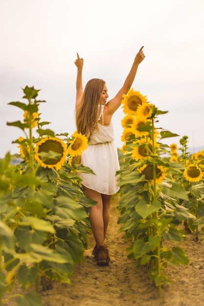 Foto vertical de uma jovem loira alegre em um campo de girassóis sob a luz do sol