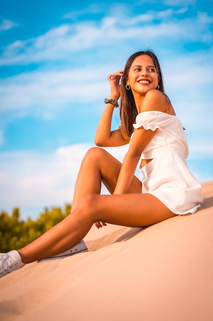 Foto vertical de uma jovem morena caucasiana curtindo as férias na praia em um vestido branco