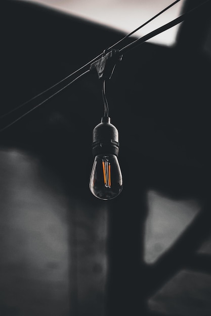 Foto vertical de uma lâmpada pendurada em um fio em um fundo escuro e embaçado