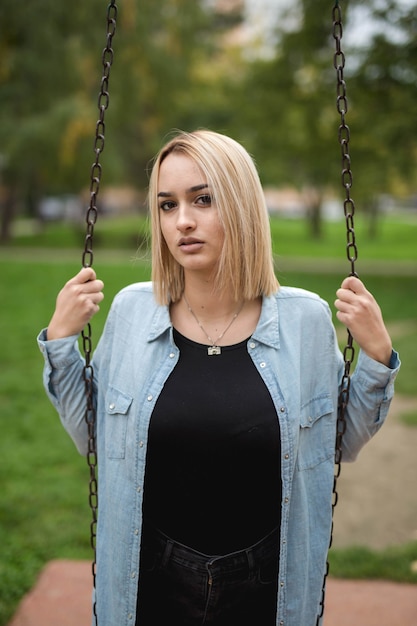 Foto vertical de uma linda mulher caucasiana em jeans segurando um balanço de metal no parque