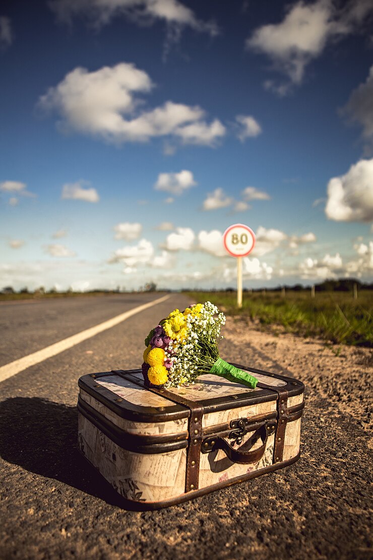 Foto grátis foto vertical de uma mala vintage com um buquê em uma estrada vazia