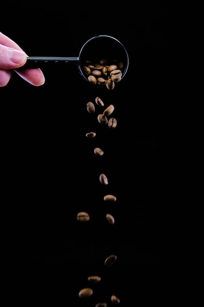 Foto vertical de uma mão humana derramando grãos de café de uma colher no preto