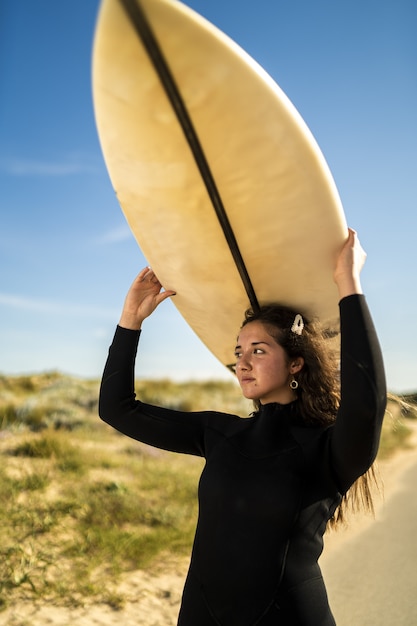 Foto grátis foto vertical de uma mulher atraente carregando uma prancha de surf acima da cabeça