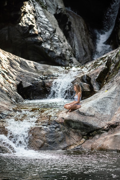 Foto vertical de uma mulher meditando perto de uma cachoeira