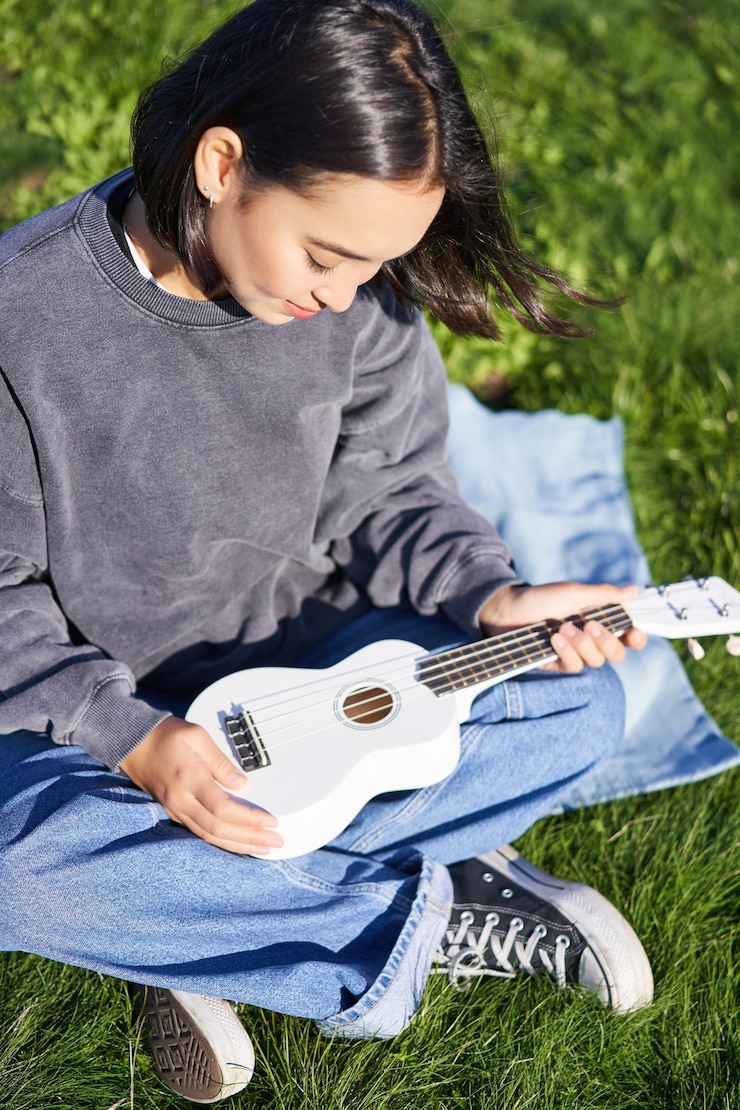 Foto grátis foto vertical de uma musicista olhando com cuidado para sua guitarra ukulele branca tocando música no parque s