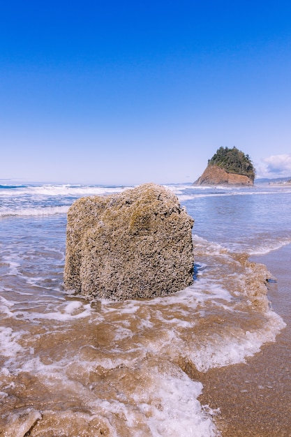 Foto vertical de uma pedra no oceano sob um céu azul claro