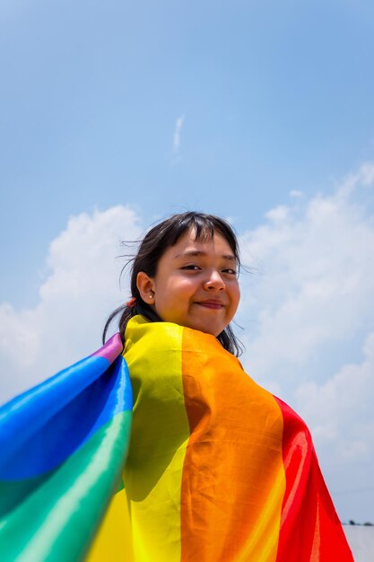 Foto vertical de uma pequena menina sorridente com uma bandeira de arco-íris