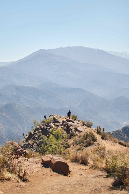 Foto vertical de uma pessoa caminhando de volta da borda de uma montanha ao longe